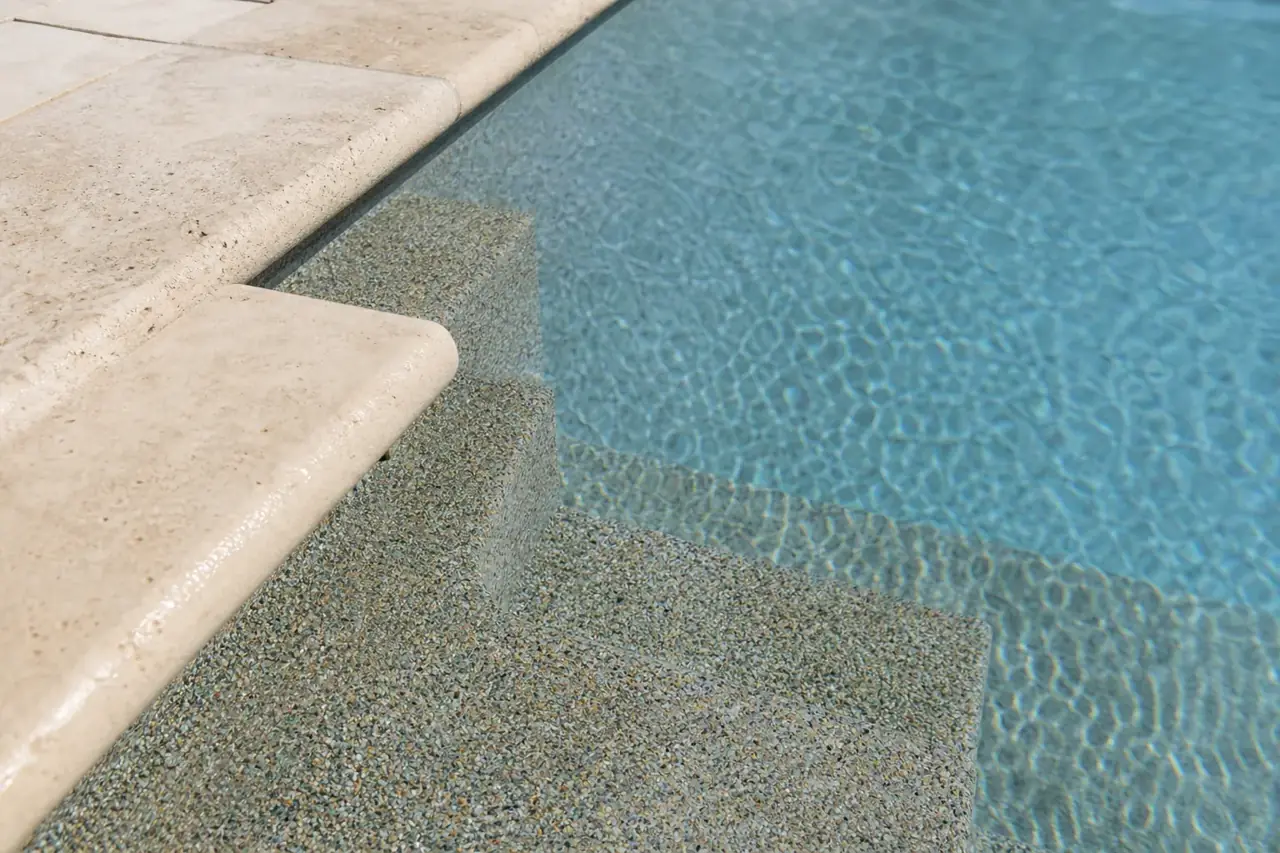 Fresh pebble plaster surface meeting travertine coping